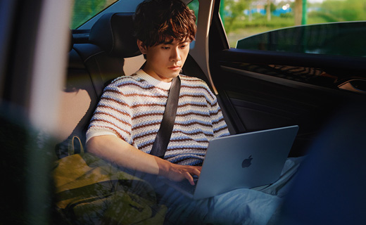 照片展示一個(gè)男生坐在轎車后排用著 MacBook Air。