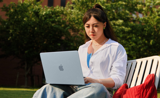 照片展示一位女生坐在草坪邊的長(zhǎng)椅上用著 MacBook Air。