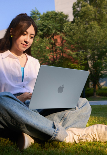 一名學(xué)生坐在戶外。她腿上放著 MacBook。