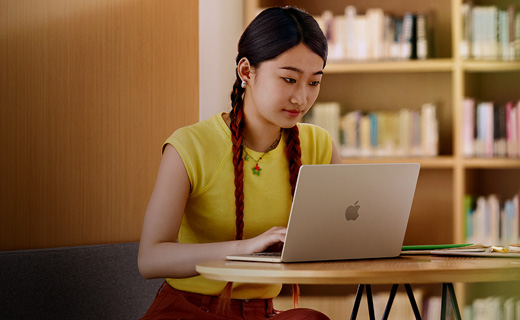 照片展示大學(xué)圖書(shū)館里，一位女生正坐在書(shū)桌前用著 MacBook Air。