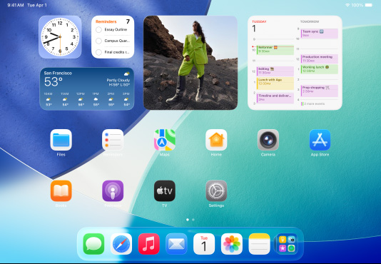 三款 iPad 機(jī)型橫屏放置，中間的機(jī)型位于另外兩款前方，Apple Pencil 以磁力吸附在中間機(jī)型的頂部；中間屏幕顯示主屏幕，展示具有 Liquid Glass 效果的彩色 app 圖標(biāo)；左側(cè)屏幕展示預(yù)覽 app；右側(cè)屏幕展示主屏幕，多個文件從程序塢呈扇狀展開。