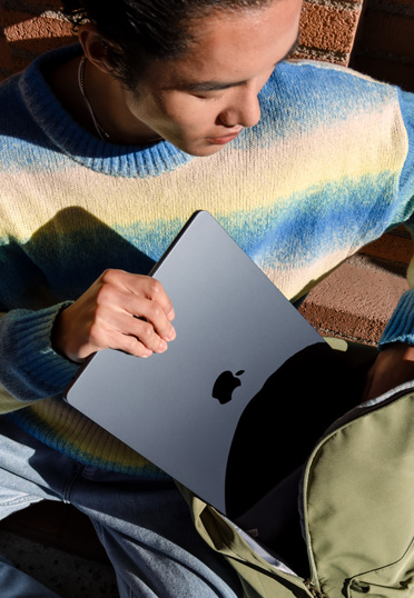一名學生坐在外面。他從書包里拿出一臺封閉的 MacBook。